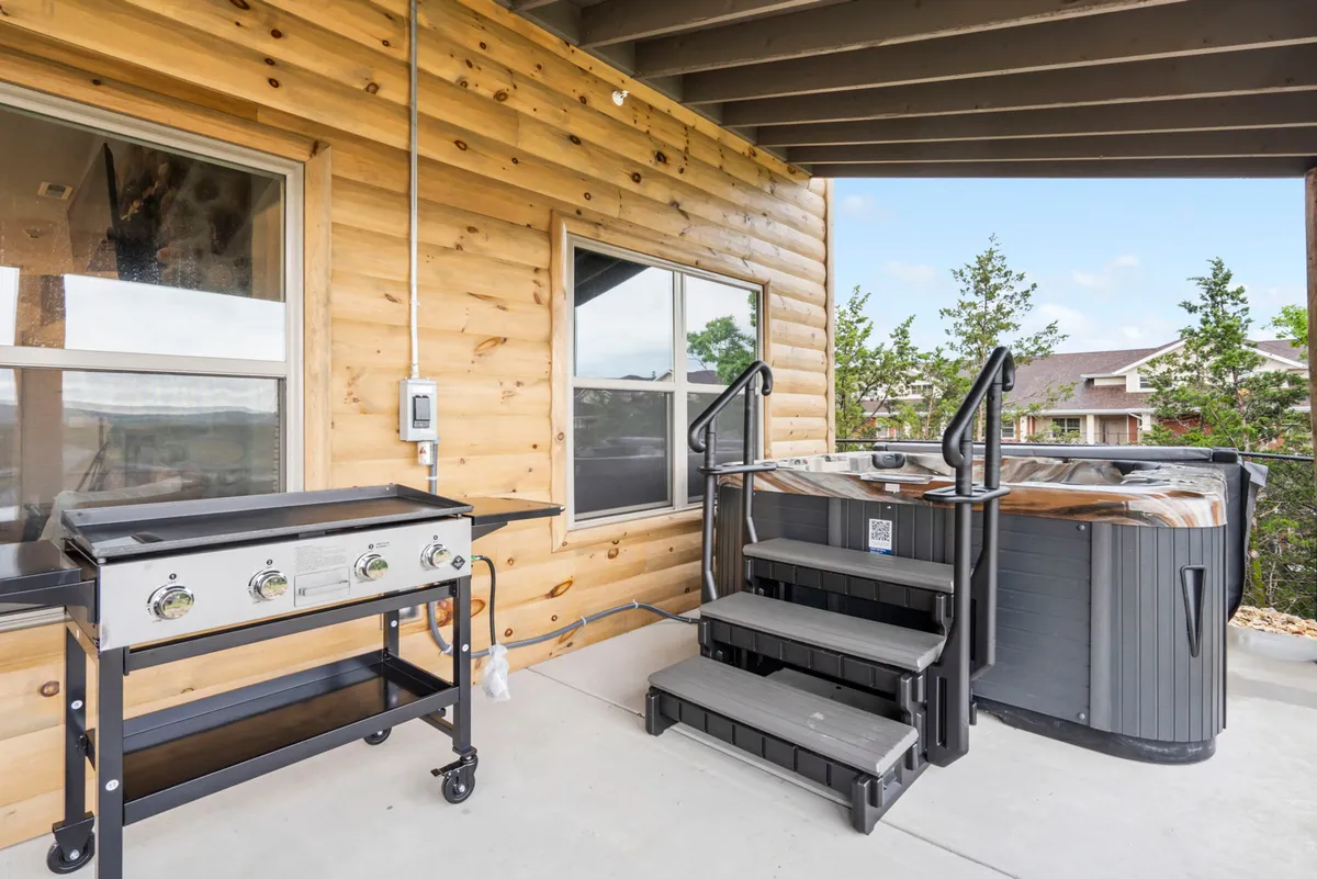 An inviting outdoor setting featuring a private hot tub and grill on a wooden deck, with steps leading up to the cozy space. The area is surrounded by greenery, highlighting the opportunity for relaxation and social gatherings after a day exploring the city.