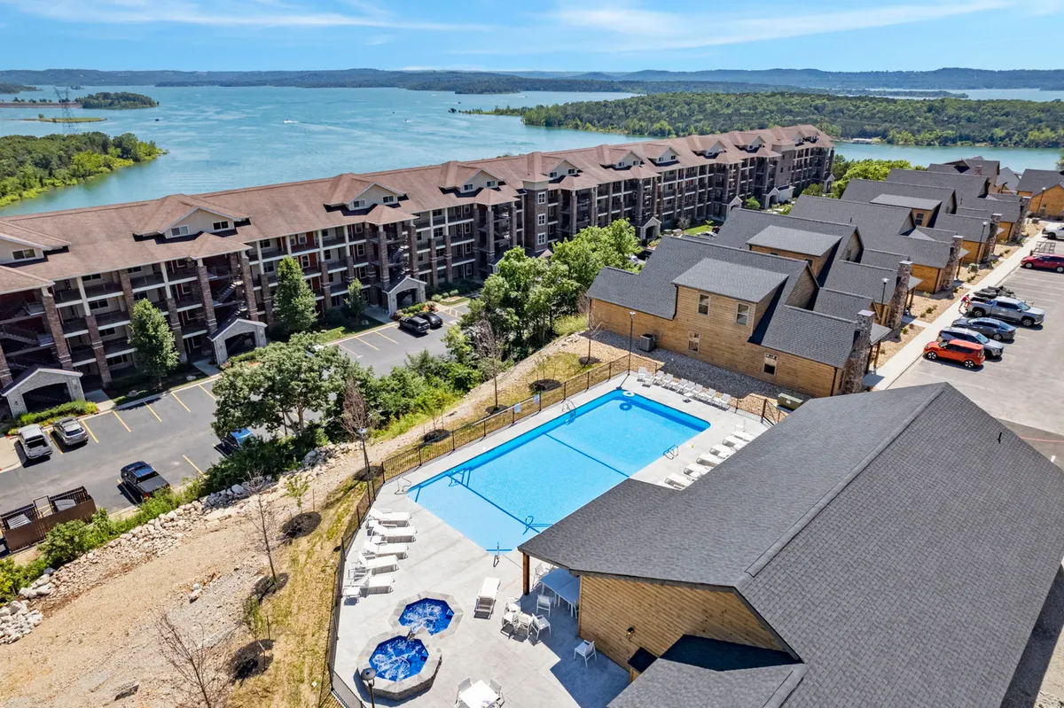 A vibrant outdoor pool and hot tub area with a direct view of the waterfront, surrounded by residential buildings and greenery. The space is set up for swimming, lounging, and enjoying the outdoors, capturing a lively yet relaxing resort-like atmosphere.