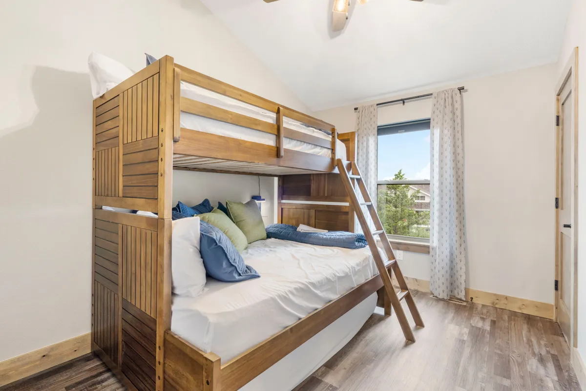 A playful bunk room featuring a bunk bed with decorative pillows, a bright window view, and a cozy, relaxed vibe perfect for kids. The arrangement suggests space for both sleep and imaginative play.