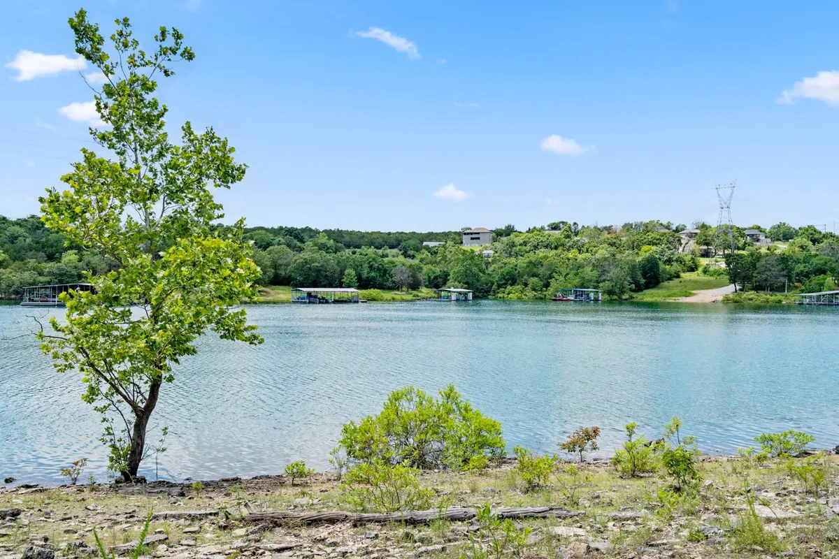 A tranquil lakeside scene featuring Table Rock Lake, a nearby tree, distant houses, and a gently winding path leading down to the water. The natural setting invites activities like boating, fishing, picnicking, or quiet reflection, supporting the resort's lakeside location and outdoor adventures.