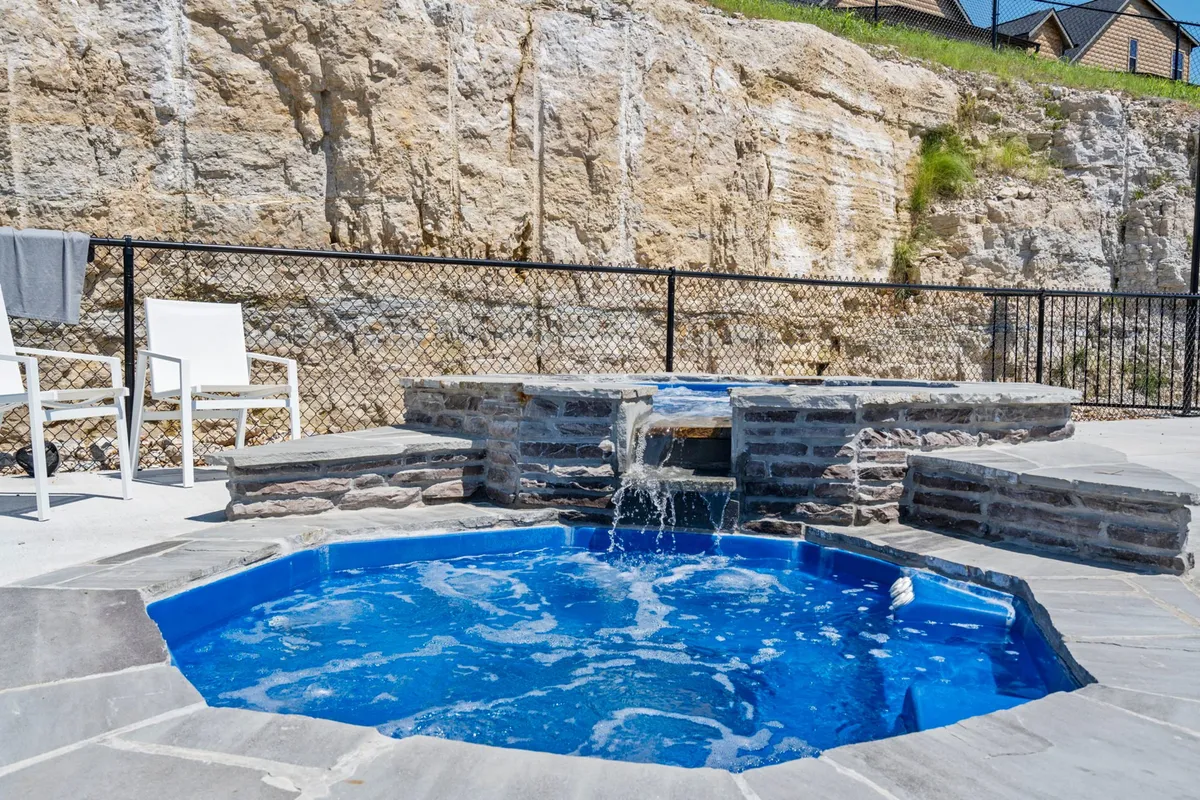 This image showcases a stylish outdoor hot tub set among natural rock features and surrounded by lounge chairs, with lush landscape and sunset views in the background. The setting is ideal for post-golf relaxation and socializing in a serene environment.