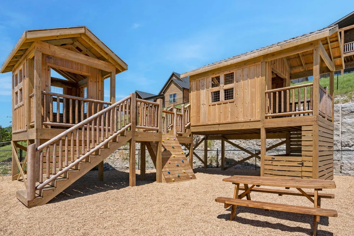 A colorful playhouse structure complete with a slide, climbing wall, and picnic table set in a grassy outdoor area. Children are pictured playing and laughing, highlighting the space's family-friendly vibe and potential for imaginative adventures.