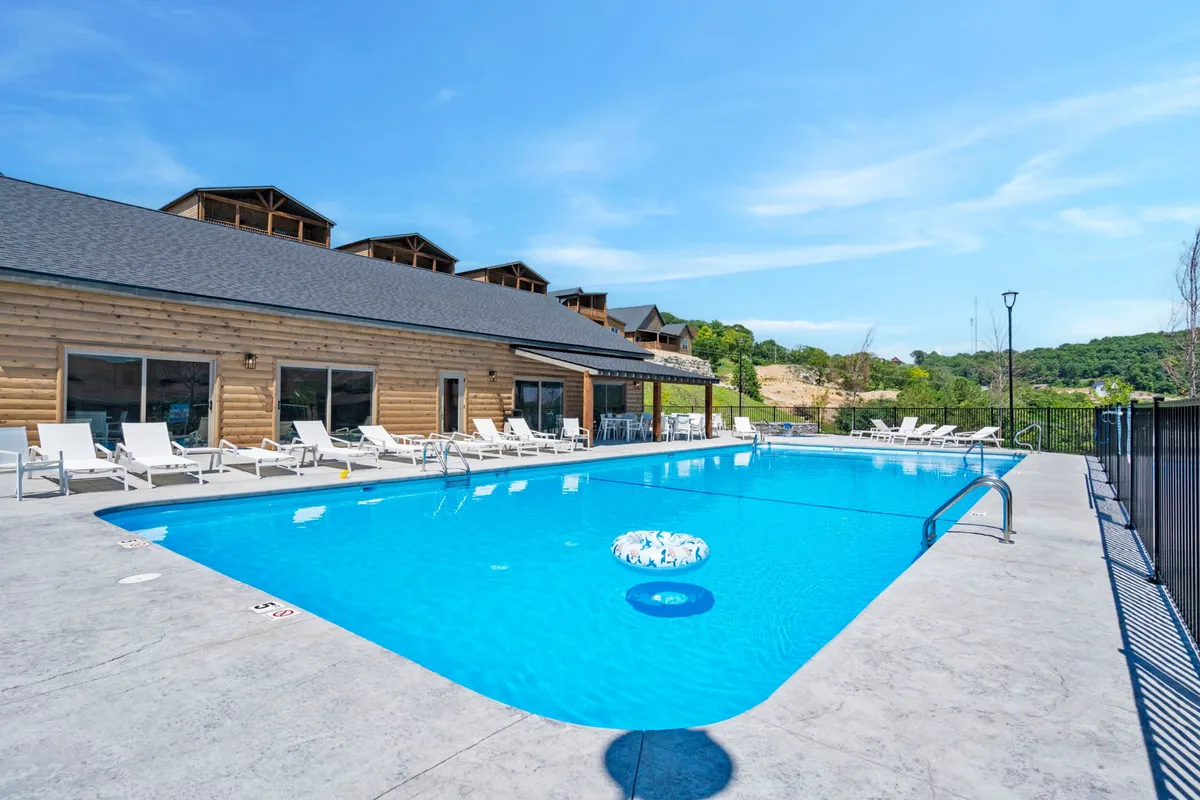 This image displays an outdoor swimming pool with lounge chairs and a wooden building in the background. The relaxed atmosphere is inviting, with space for sunbathing, swimming, and informal gatherings. The scene is likely set in the late afternoon or early evening, evoking the fun and relaxation of summer days by the water.